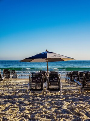 A beach with rows of Bora Bora branded lounge chairs and a large umbrella providing shade. - Bora Bora Pousada (Bombinhas)