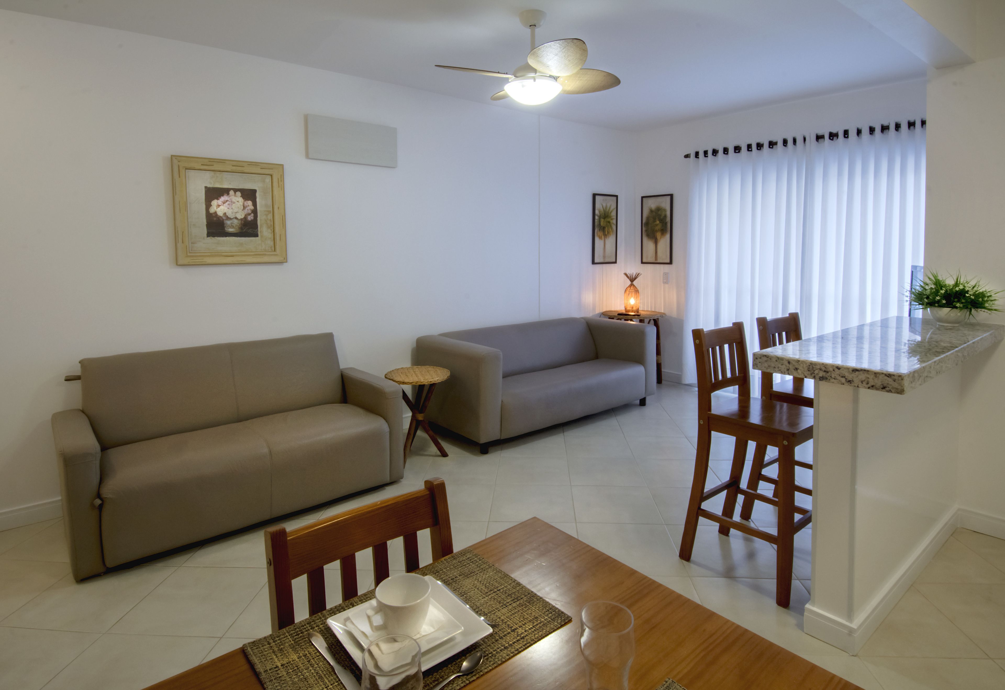 A living room with a sofa, a dining table with chairs, a ceiling fan, and a small side table with a lamp.