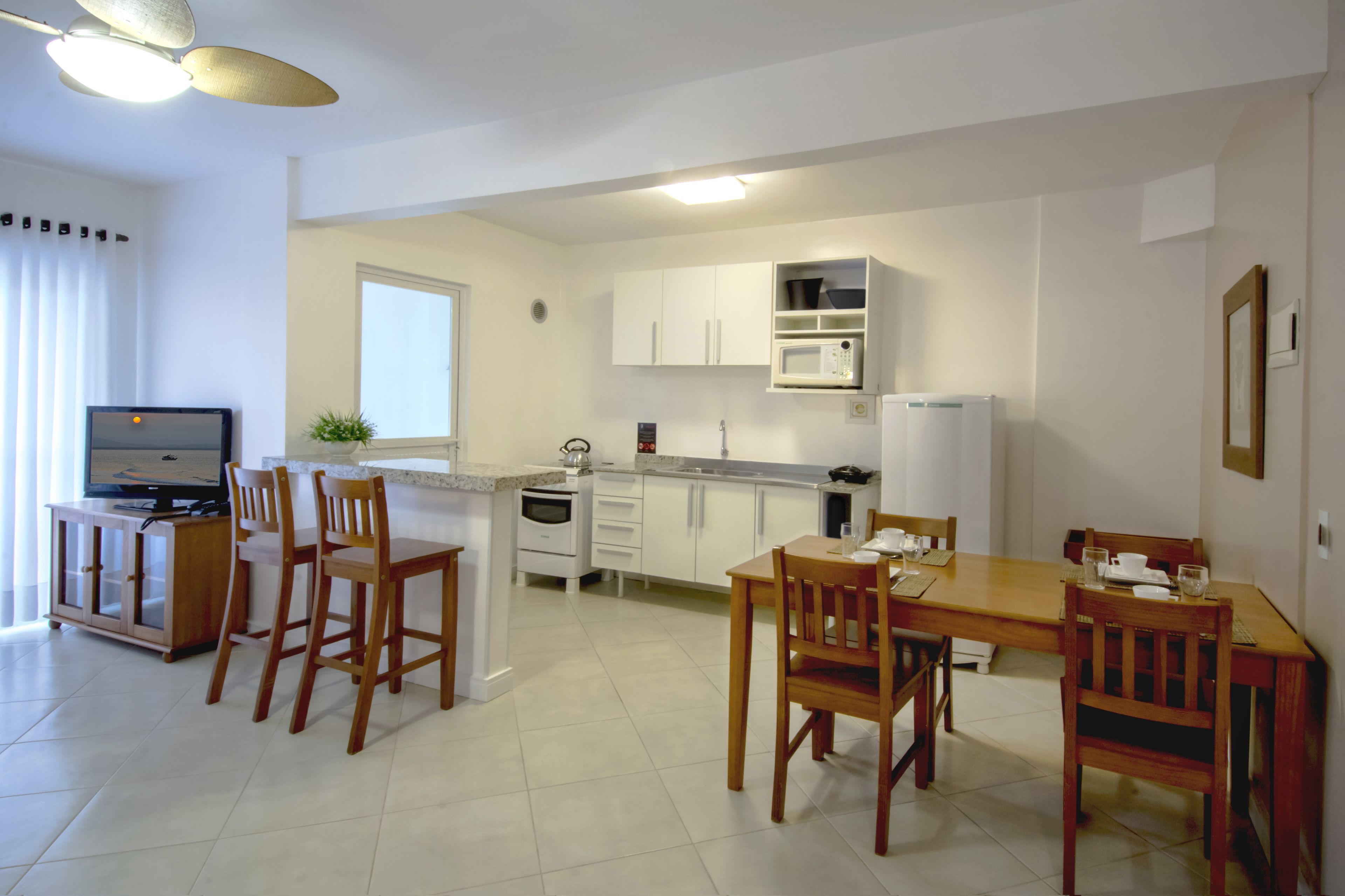 Una cocina moderna con armarios blancos, un microondas y un comedor con sillas de madera y una mesa.