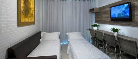 Habitación de hotel con dos camas, un televisor en la pared, un ventilador de techo y una ventana con cortinas.