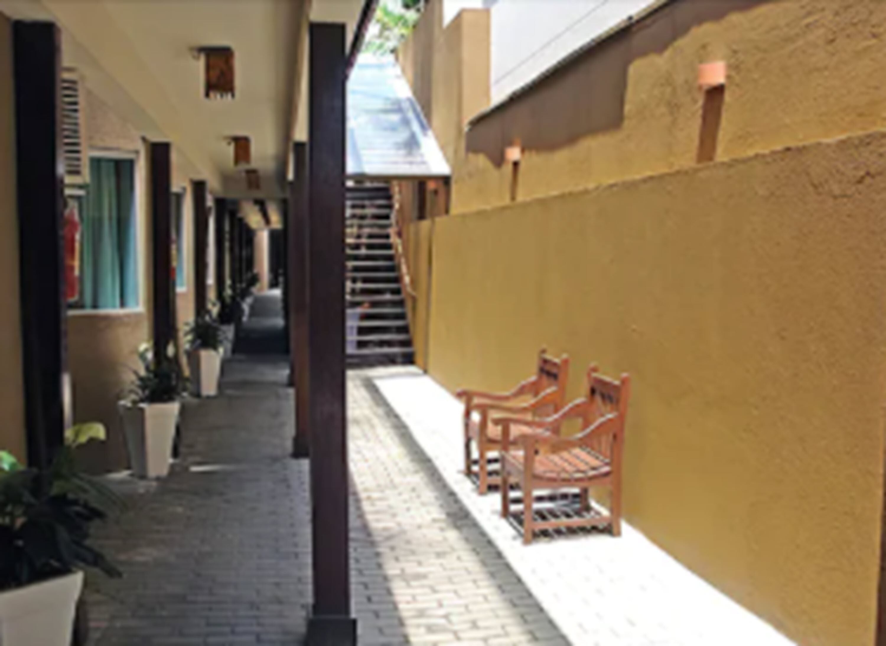 Un couloir doté d’un sol en briques, de bancs en bois, de plantes en pot et d’un escalier menant à un étage supérieur.