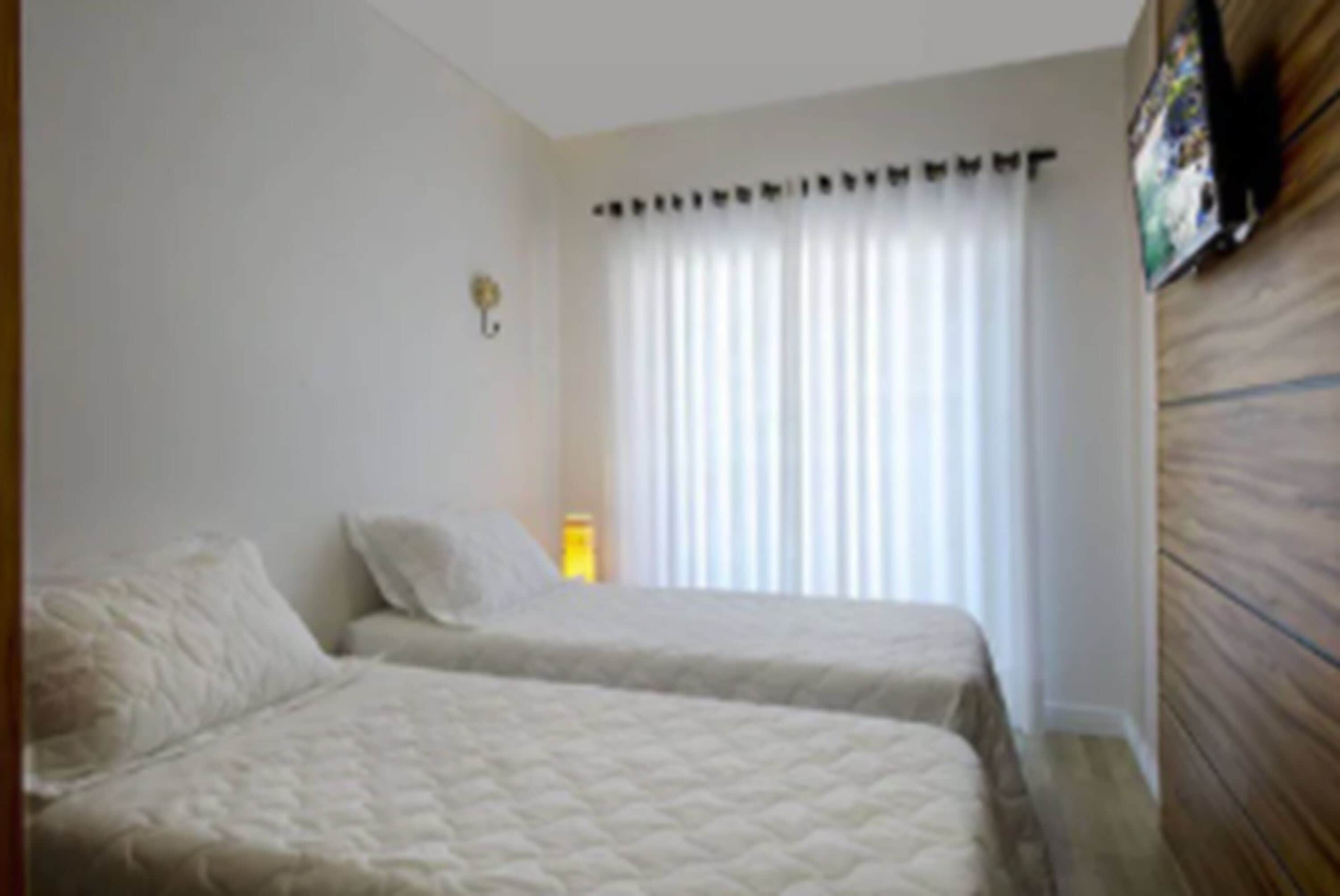 A hotel room with two beds, a large window with sheer curtains, and a wooden headboard.