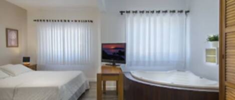 A hotel room with a bed, a TV, a small table, and a bathtub.