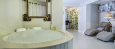 Un baño con una bañera grande, un espejo con un marco decorado, y una puerta que da a una sala de estar con un sofá y una lámpara.