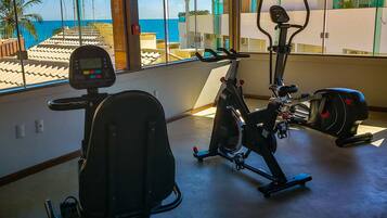 Ein Fitnessraum mit Trainingsgeräten, großen Fenstern und Meerblick.