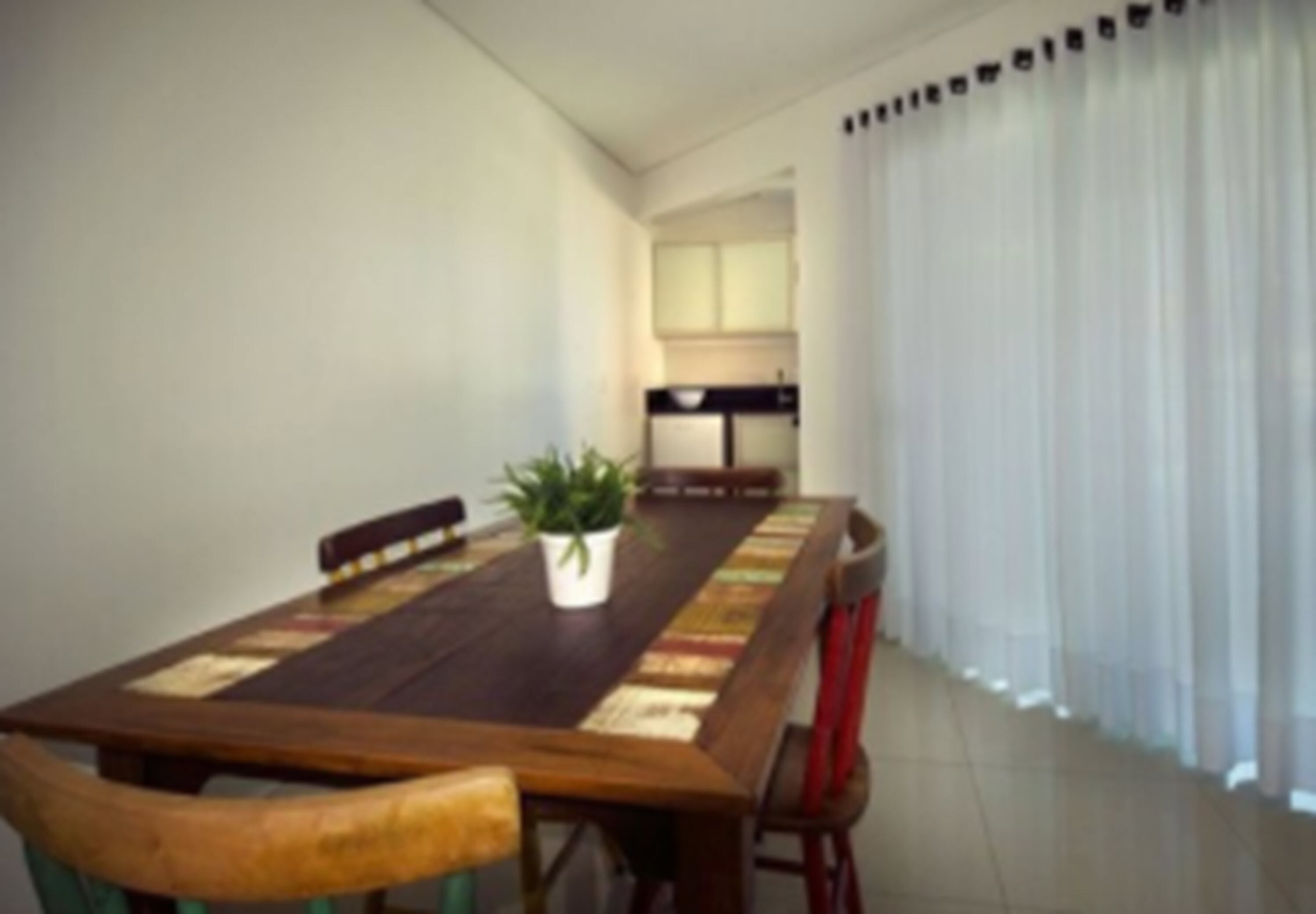 Uma sala de jantar com uma longa mesa de madeira, cadeiras e um vaso de planta.