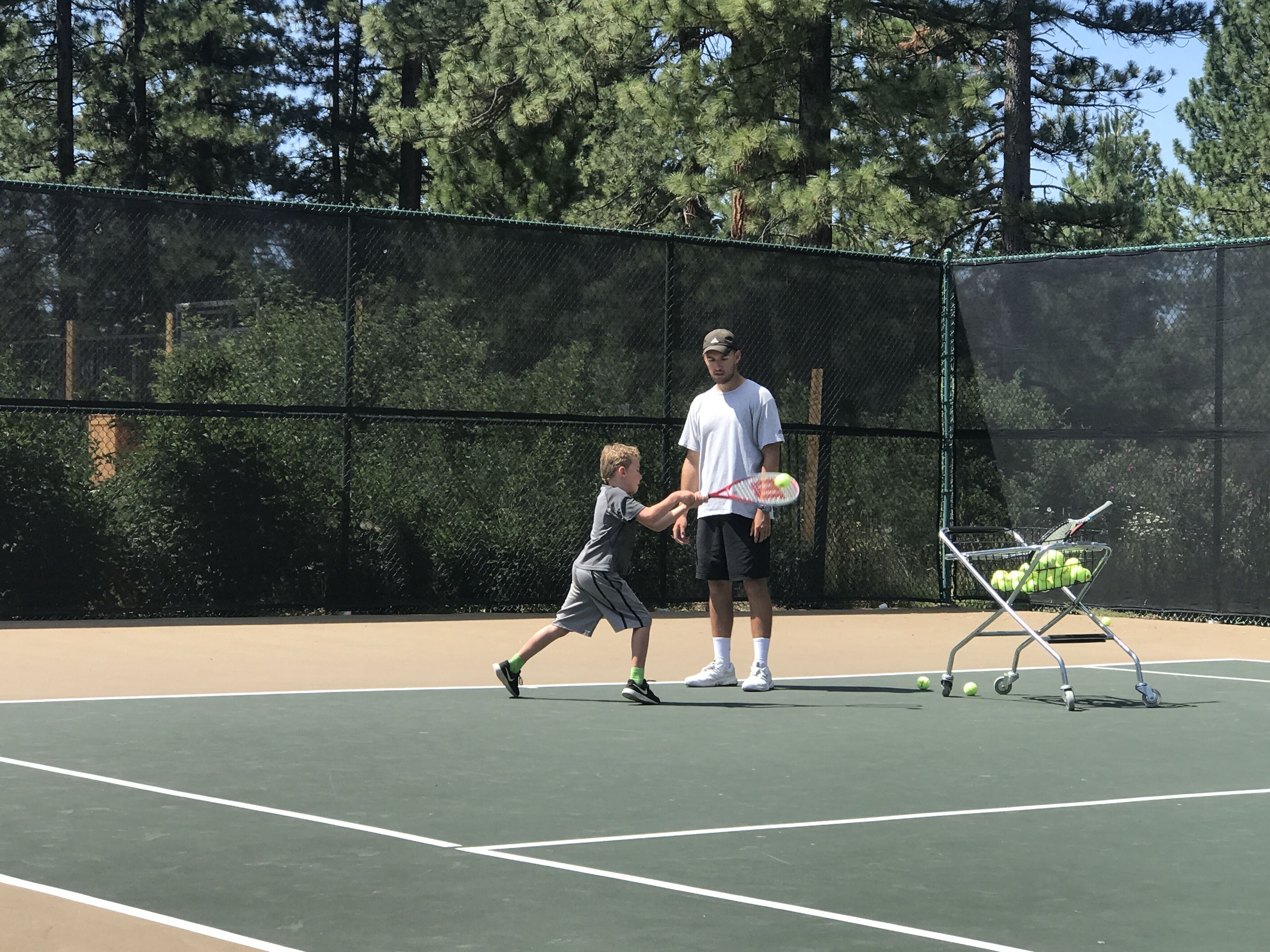 A tennis court with a net, a tennis ball, and a basket of tennis balls.