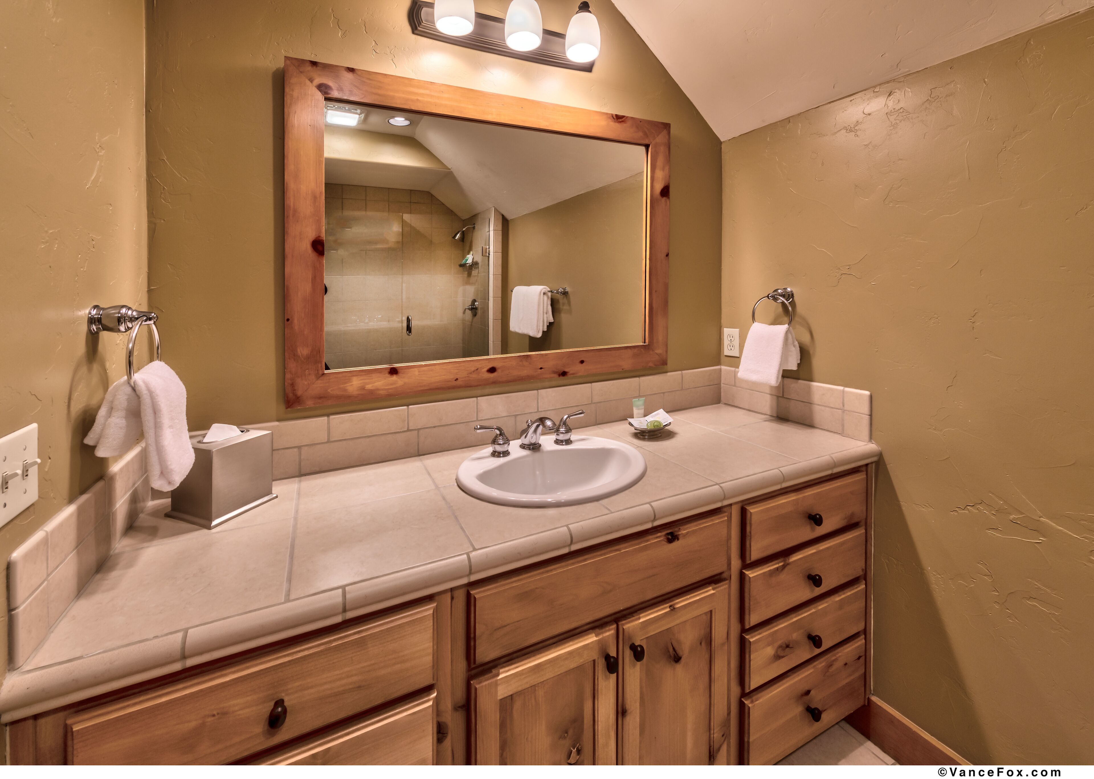 A bathroom with a wooden vanity, a large mirror, a sink, and a shower.