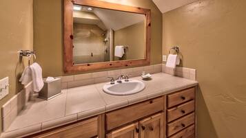 A bathroom with a wooden vanity, a large mirror, a sink, and a shower.