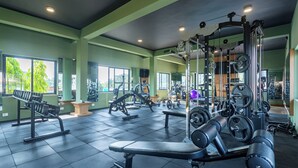 Un gimnasio con diverso equipo de ejercicio, ventanas amplias y suelo de baldosas.