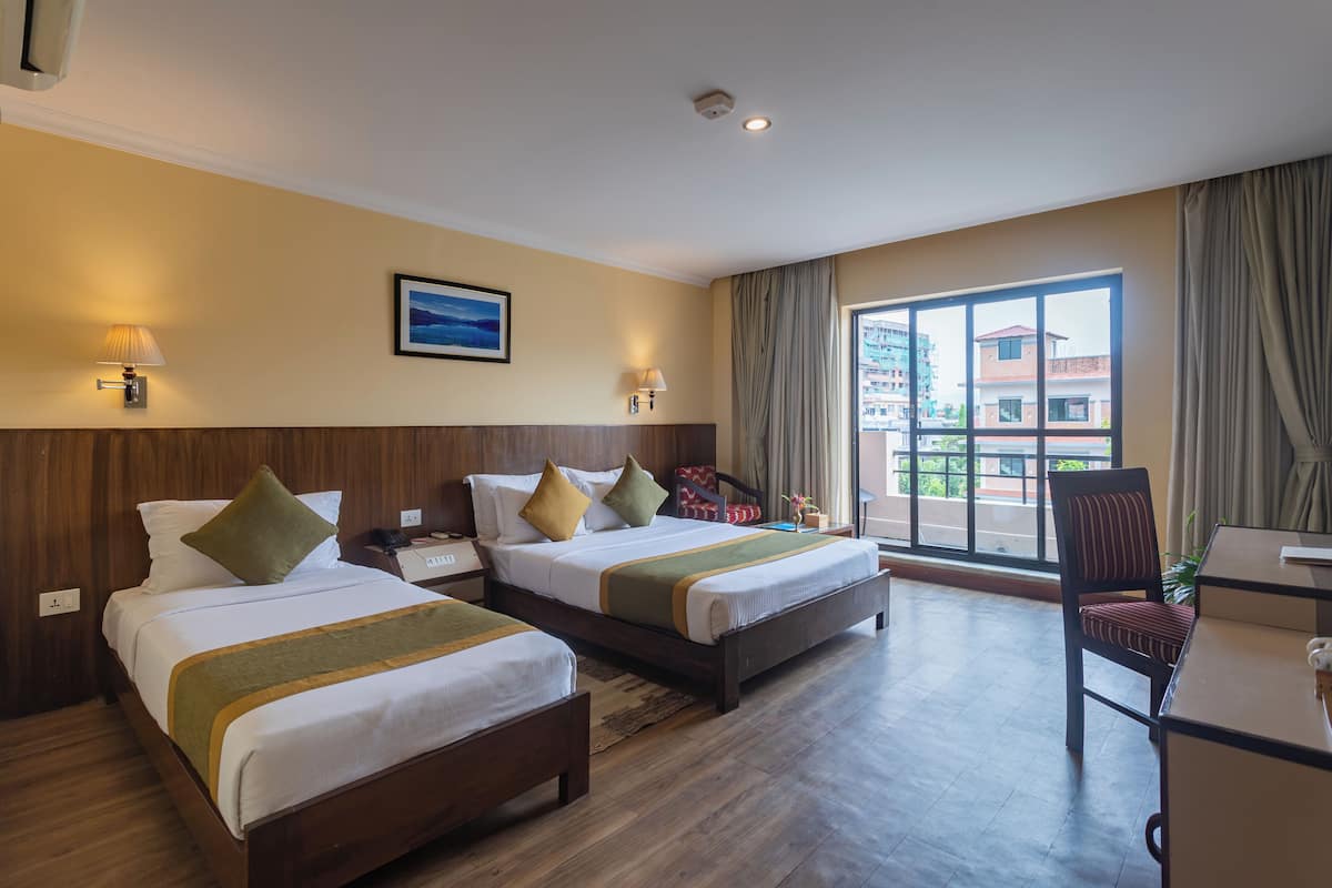 A hotel room with two beds, a desk, a chair, and a large window with a view of buildings.
