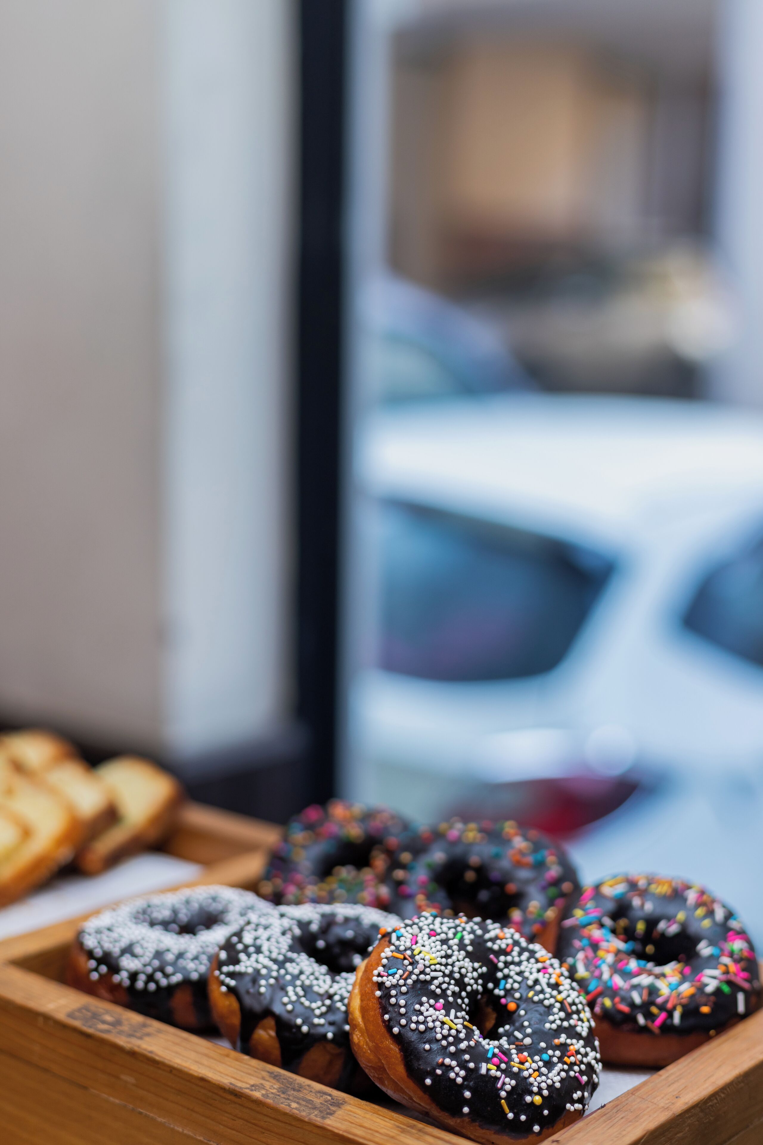 A wooden tray with assorted donuts, including chocolate and glazed varieties with sprinkles.