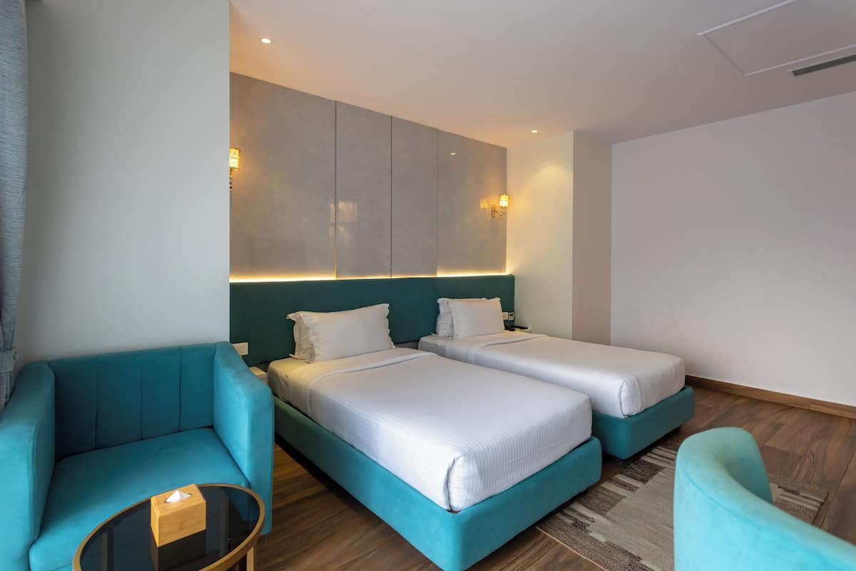 A hotel room with two beds, a sofa, a small table, and a wall-mounted light fixture.