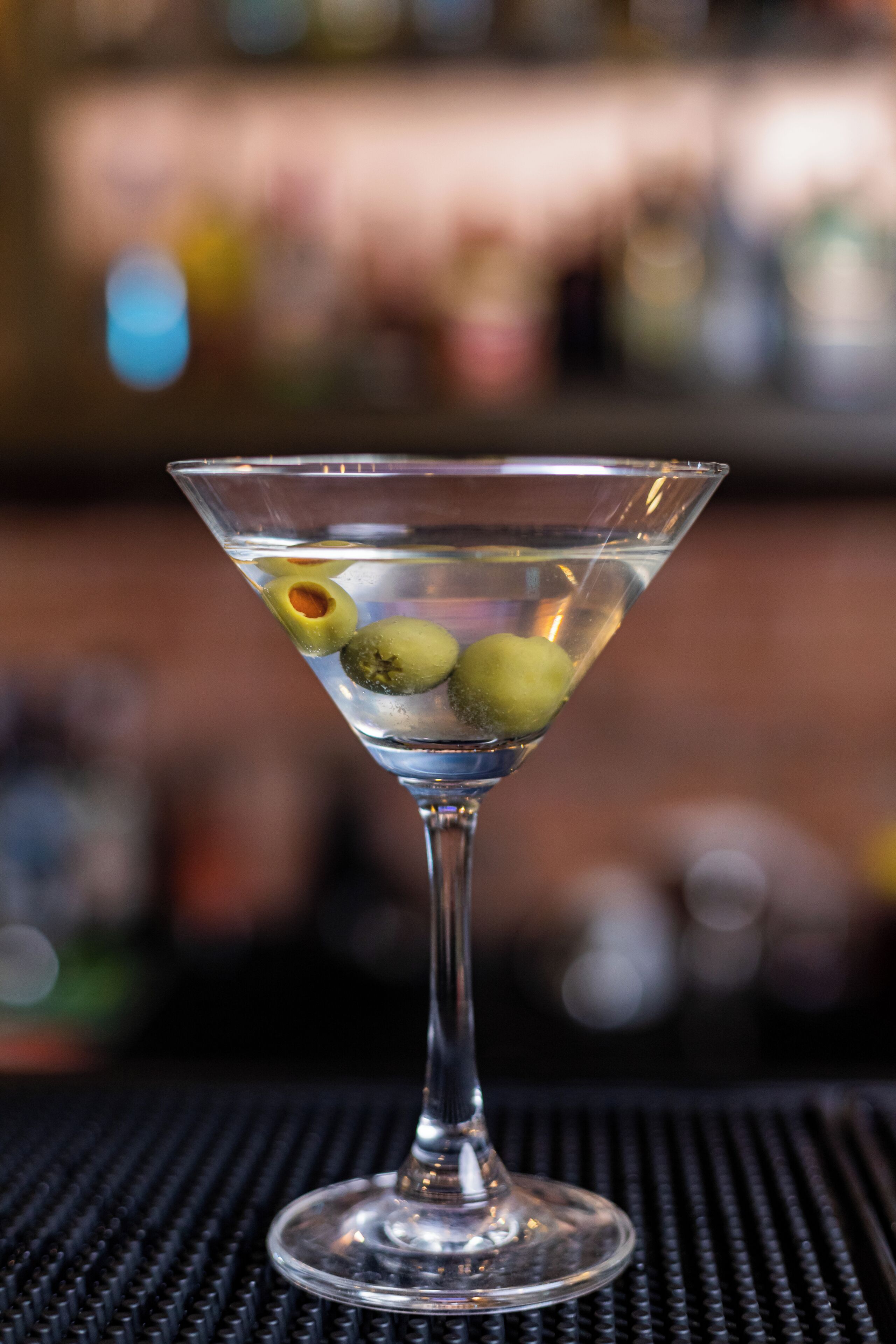A martini glass with olives on a bar counter.