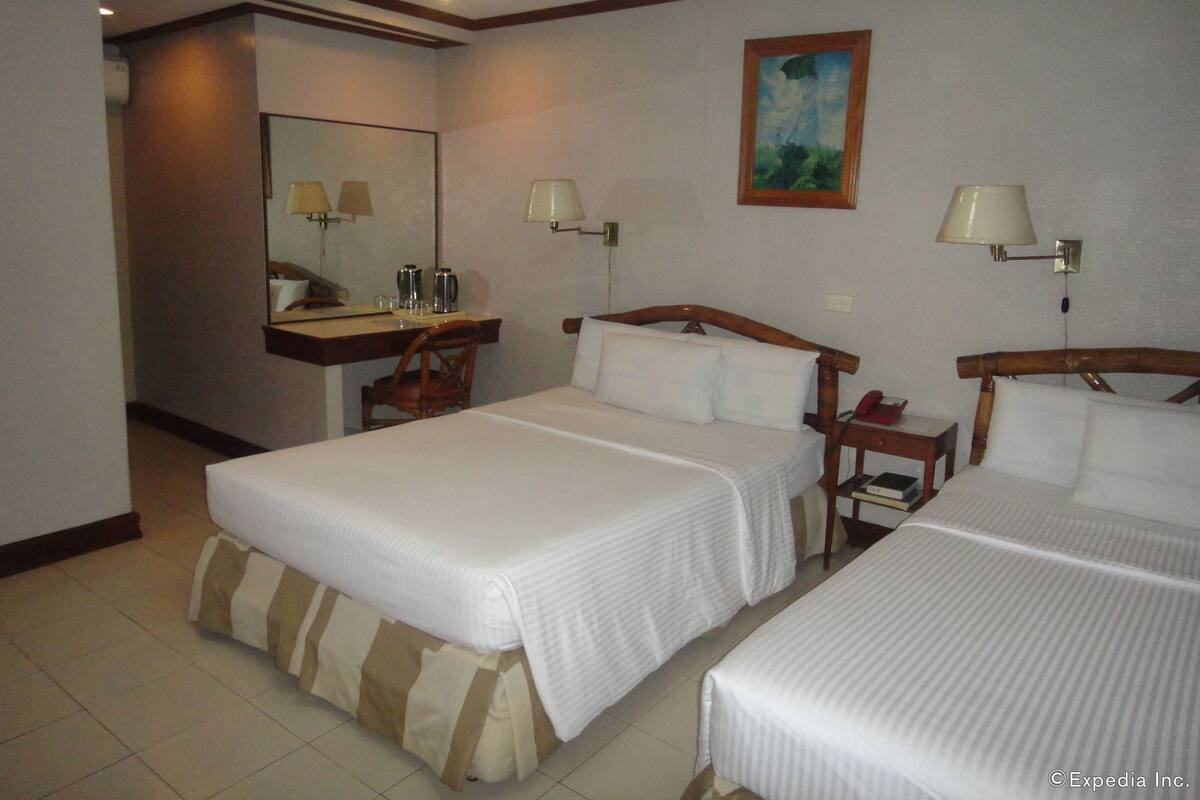 Habitación de hotel con dos camas, un escritorio con una silla, un espejo, un cuadro en la pared y dos lámparas.