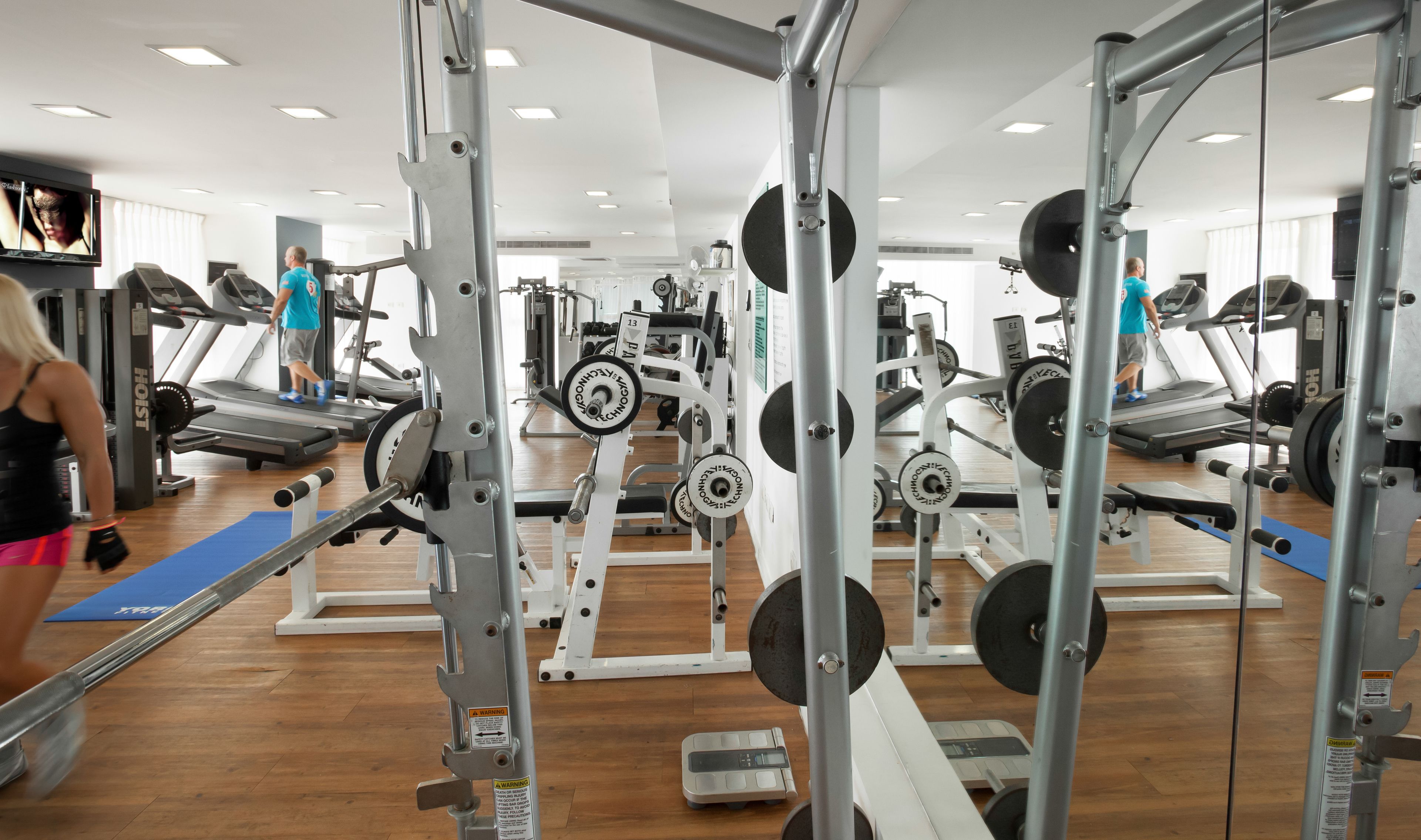 Un gimnasio con cintas de correr, máquinas de pesas y una colchoneta azul.