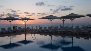 A poolside area with lounge chairs and umbrellas, overlooking the ocean at sunset.