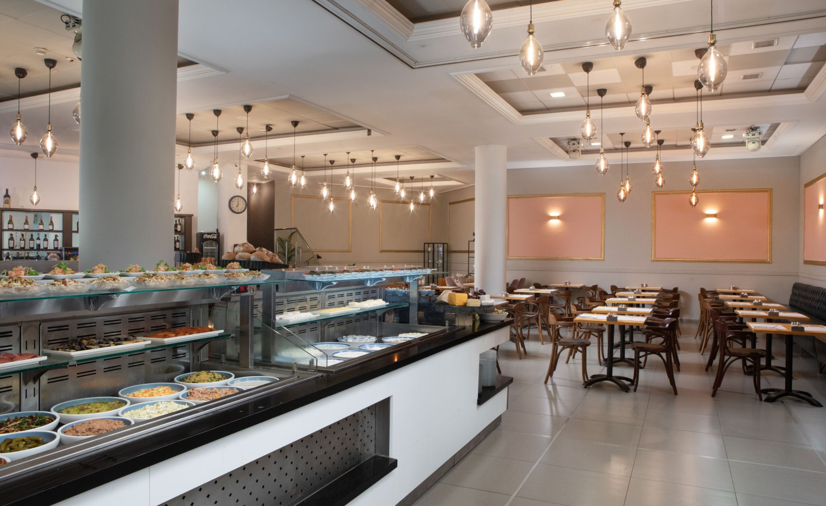 A buffet area with multiple food stations, a seating area with tables and chairs, and hanging pendant lights.
