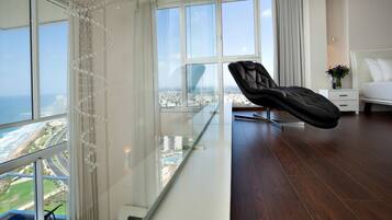 Una habitación de hotel moderna con balcón, una silla de cuero negro, cama y vistas a la ciudad y al océano.