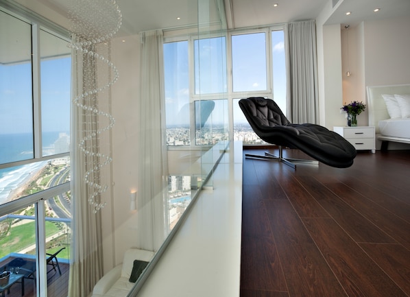 A modern hotel room with a balcony, a black leather chair, a bed, and a view of the city and ocean. - Island Luxurious Suites Hotel (Netanya)