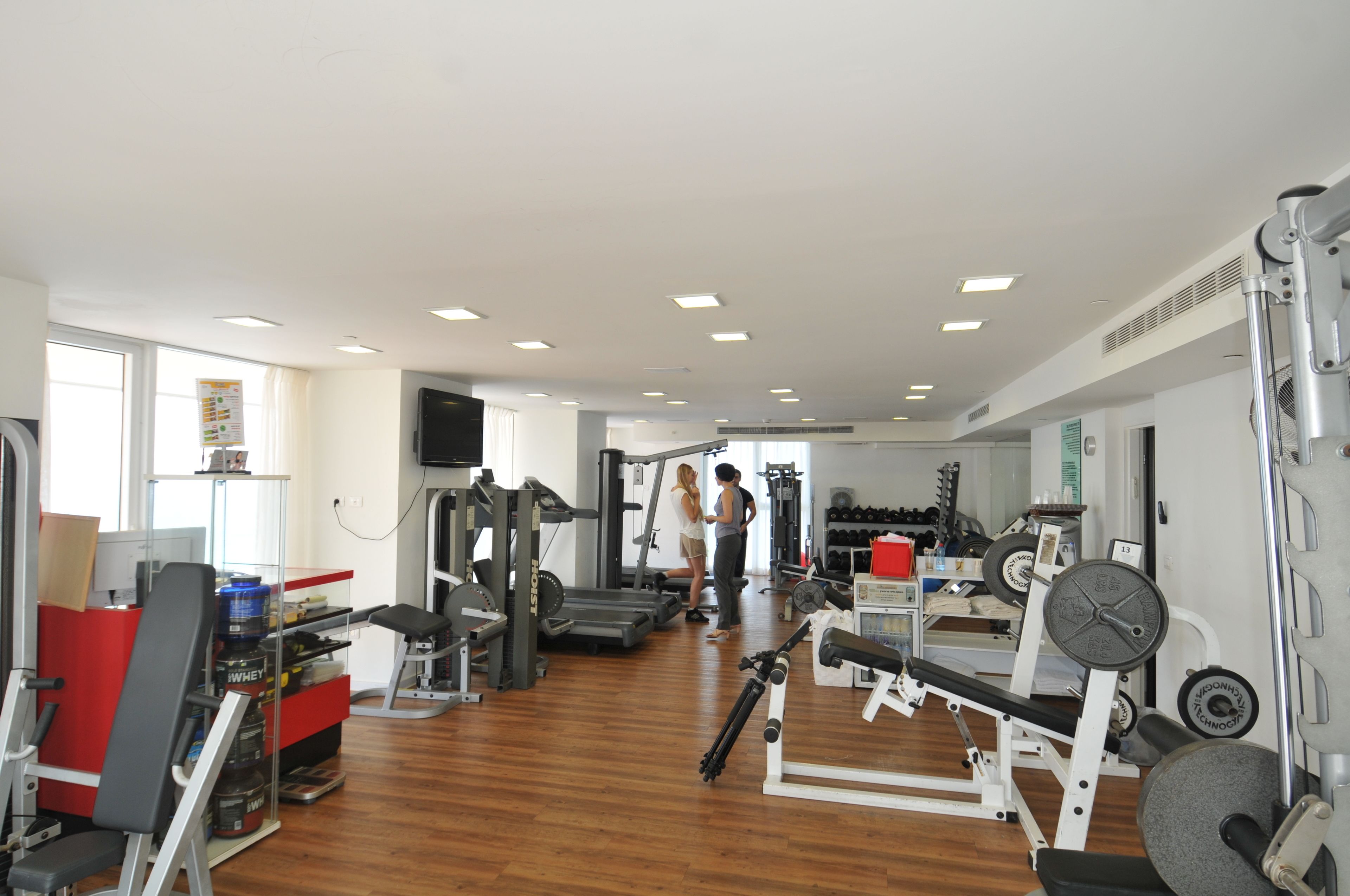 A gym with various exercise equipment, a red bench, and a weight rack.