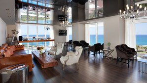 A spacious living area with a view of the sea, featuring leather sofas, white armchairs, and a wooden coffee table.