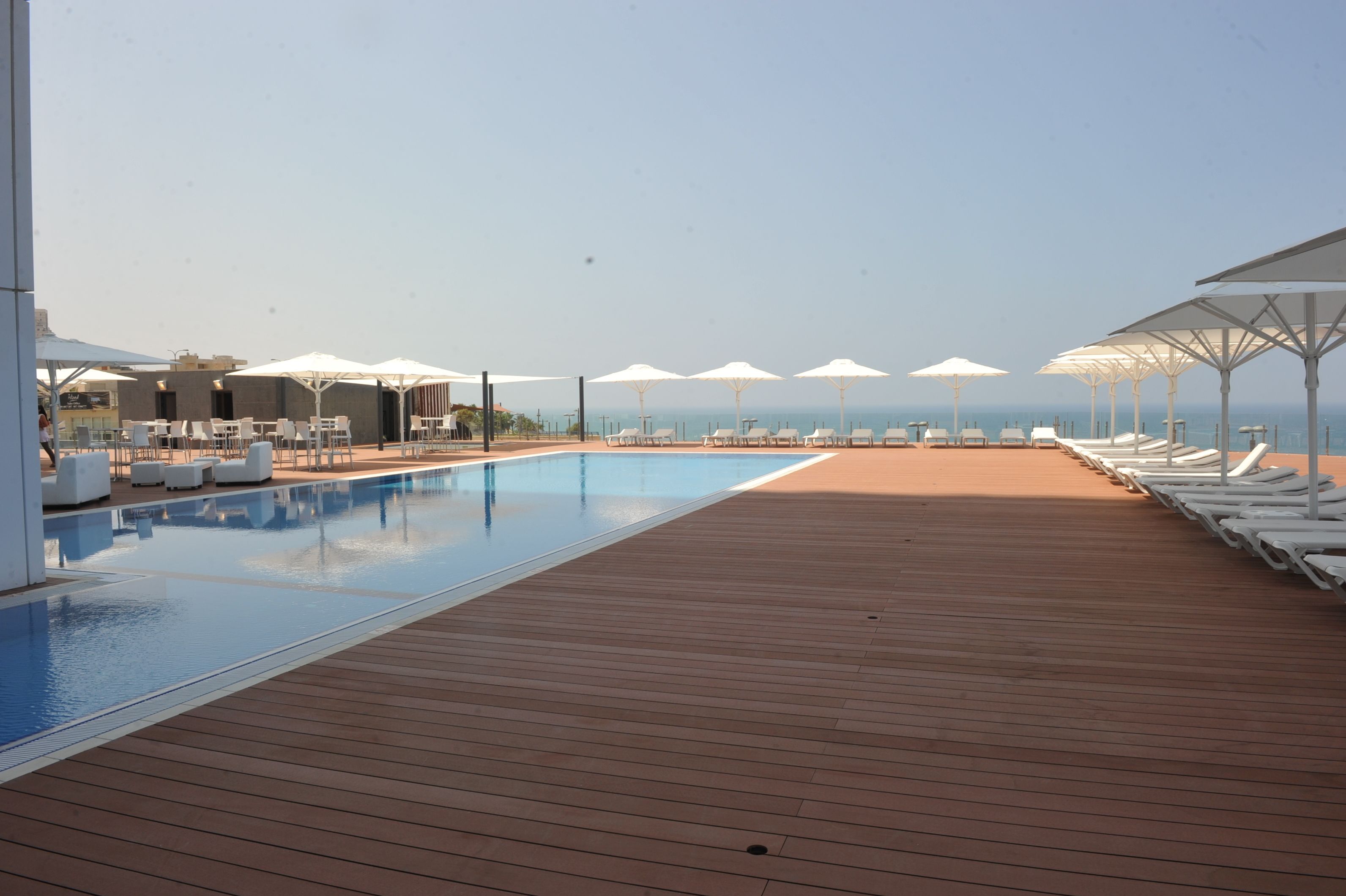 Un área junto a la piscina con sillones de descanso y sombrillas, una terraza de madera y vista al mar.