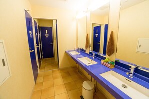 A bathroom with two sinks, a mirror, a trash can, and a towel hanging on the wall.