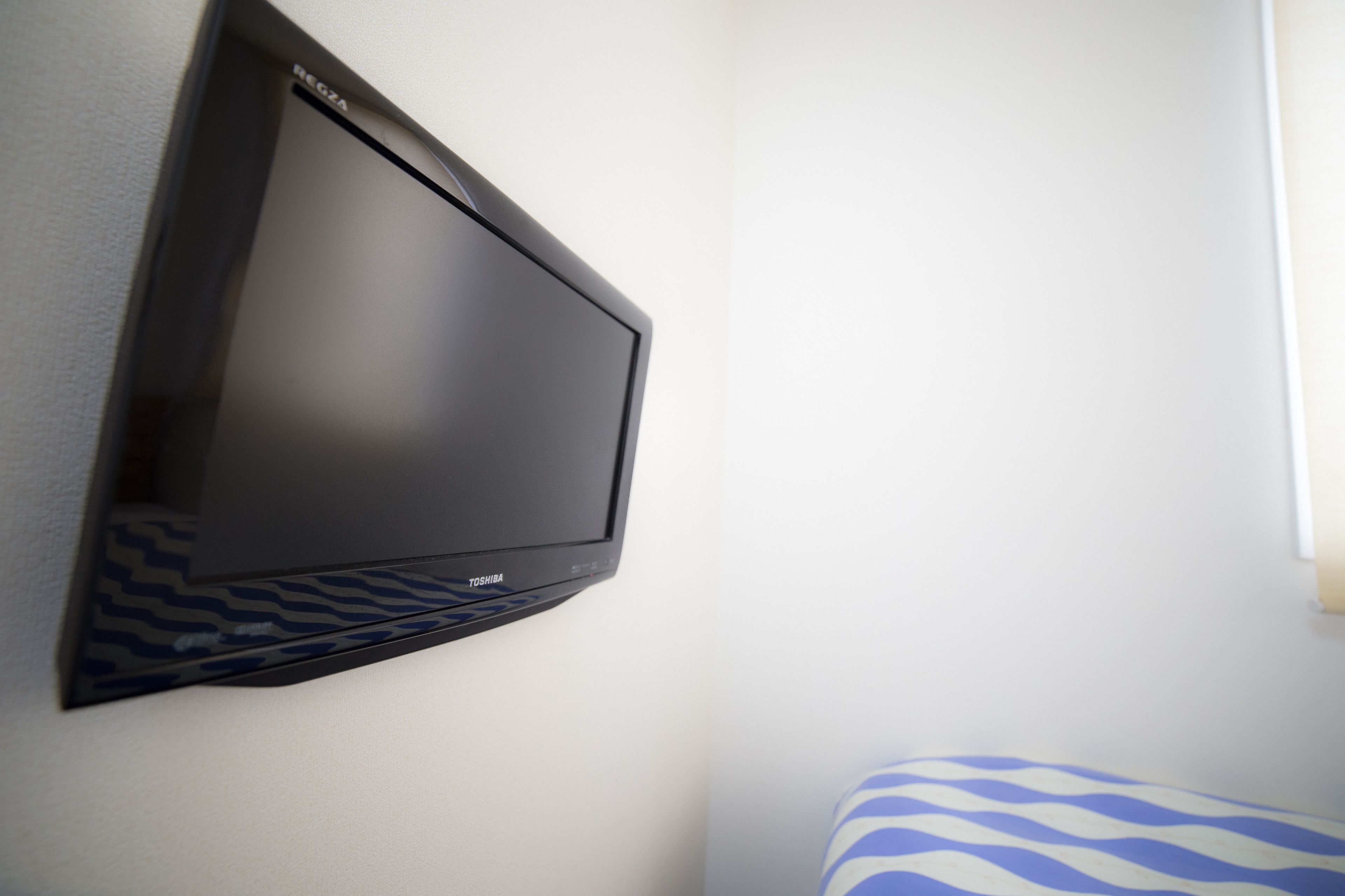 A flat-screen TV mounted on a wall, a patterned cushion, and a window with natural light.