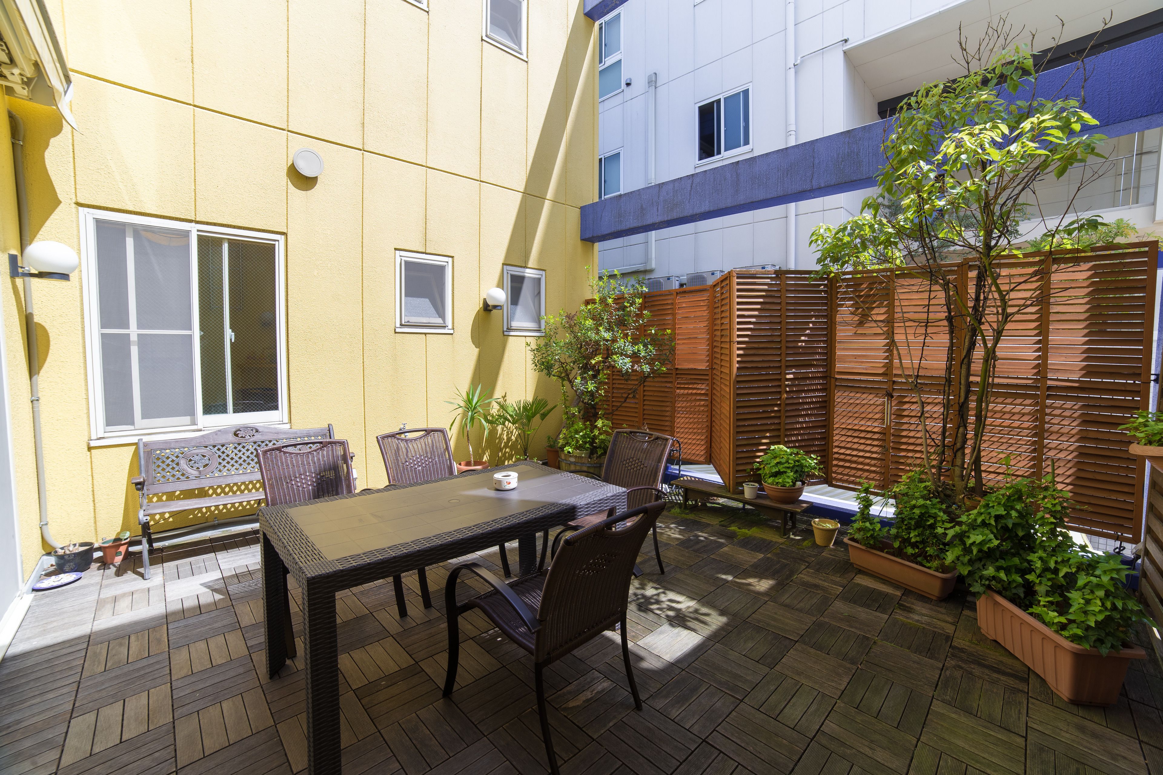 A patio with a table and chairs, a wooden fence, and potted plants.