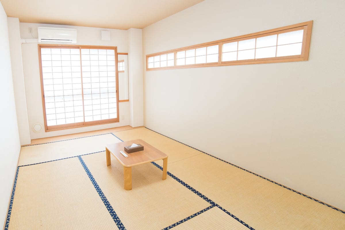 A room with tatami mat flooring, a small wooden table, a sliding shoji screen door, and a window with a wooden frame.