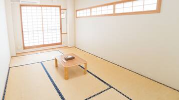 Une pièce avec un sol recouvert de tatamis, une petite table en bois, une porte coulissante de type shoji et une fenêtre avec un cadre en bois.