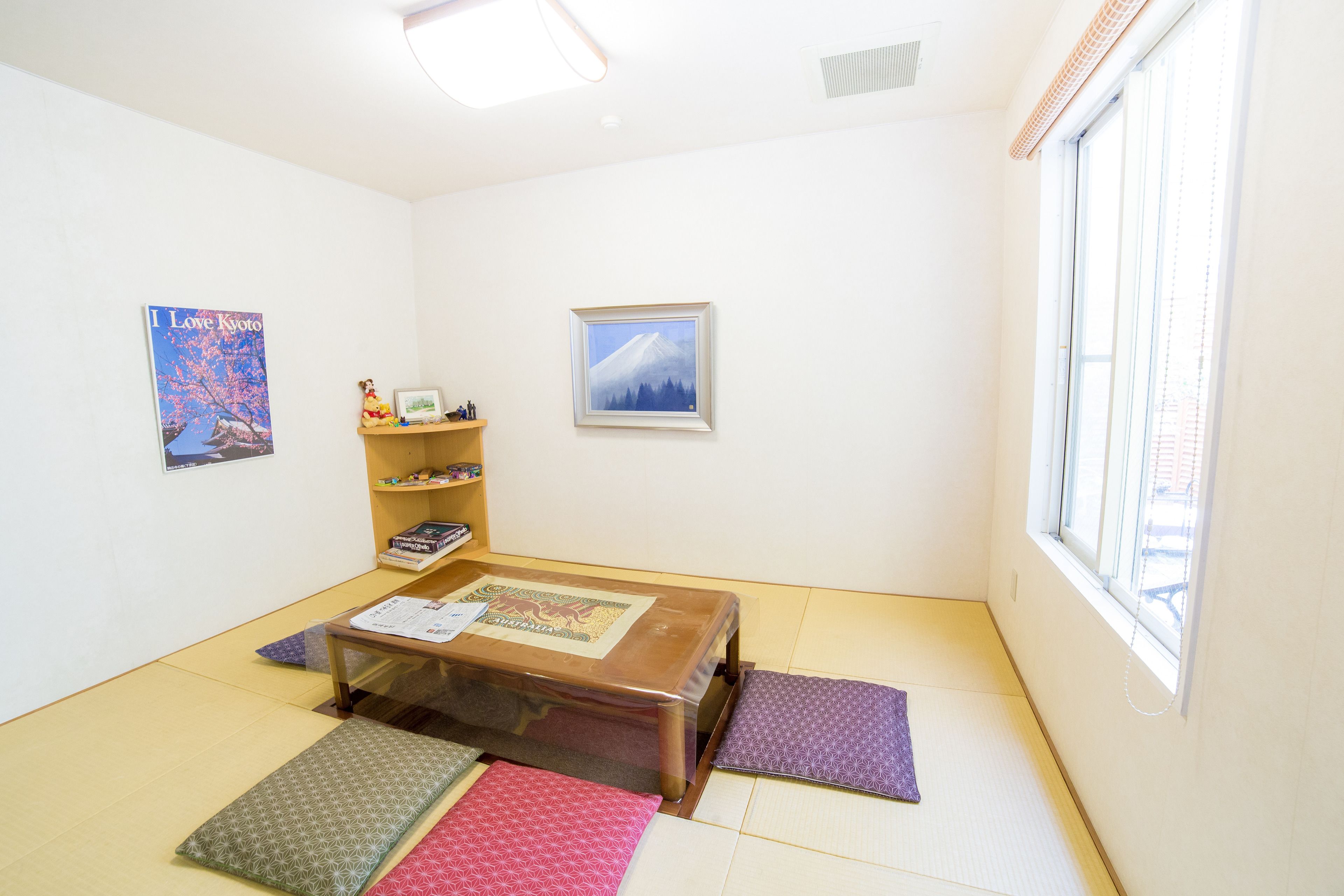 A room with tatami mats, a low wooden table, and a window with blinds.