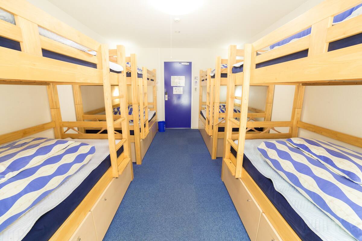 A corridor with bunk beds on either side, a blue carpet, and a door at the end.