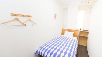 A small, neatly arranged bedroom with a bed, wooden hanger rack, and a small bedside table.