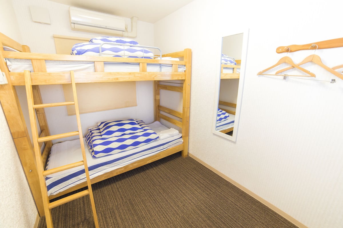 A bunk bed room with a ladder, a mirror, and wooden hangers on the wall.