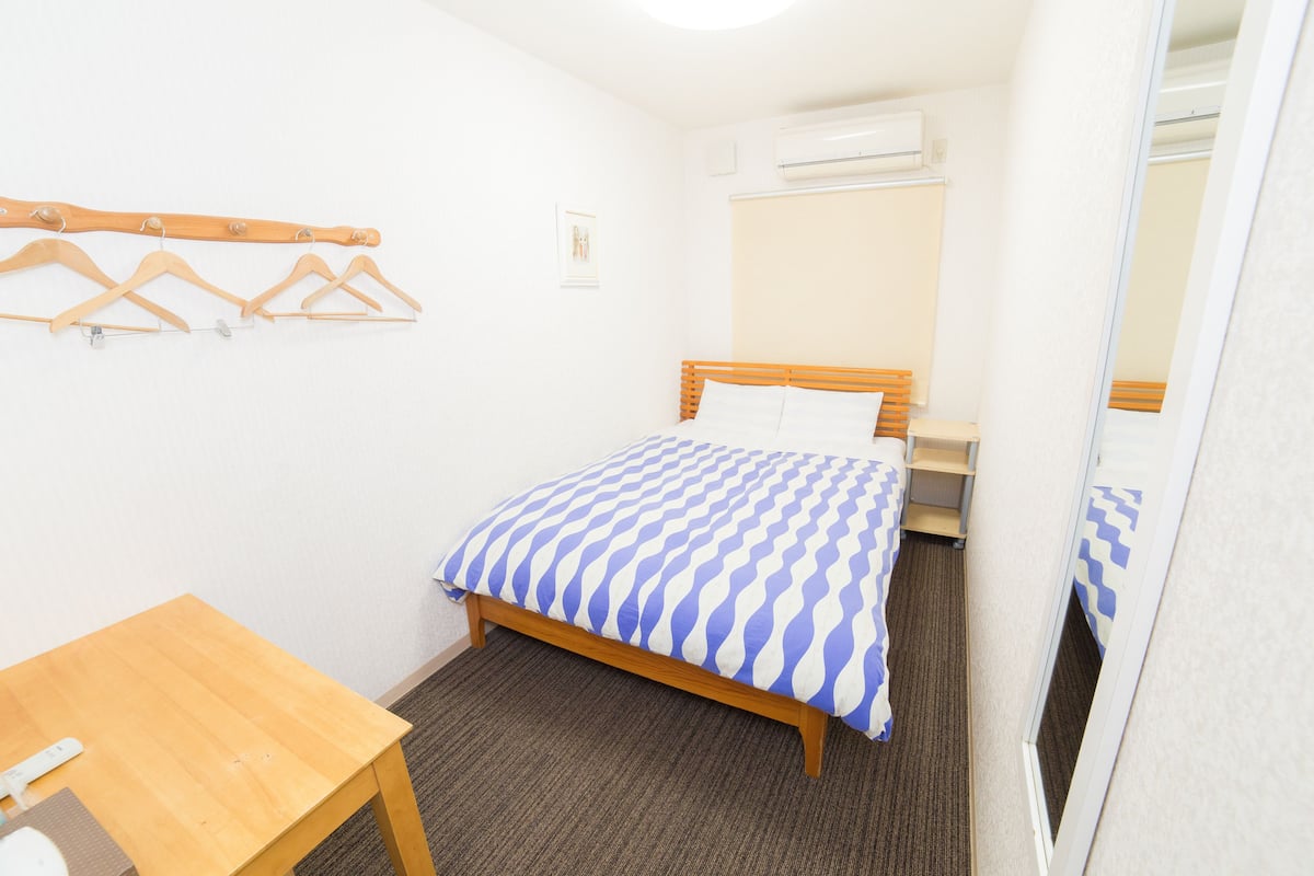 A small, neatly arranged hotel room with a single bed, a wooden table, and a mirror.
