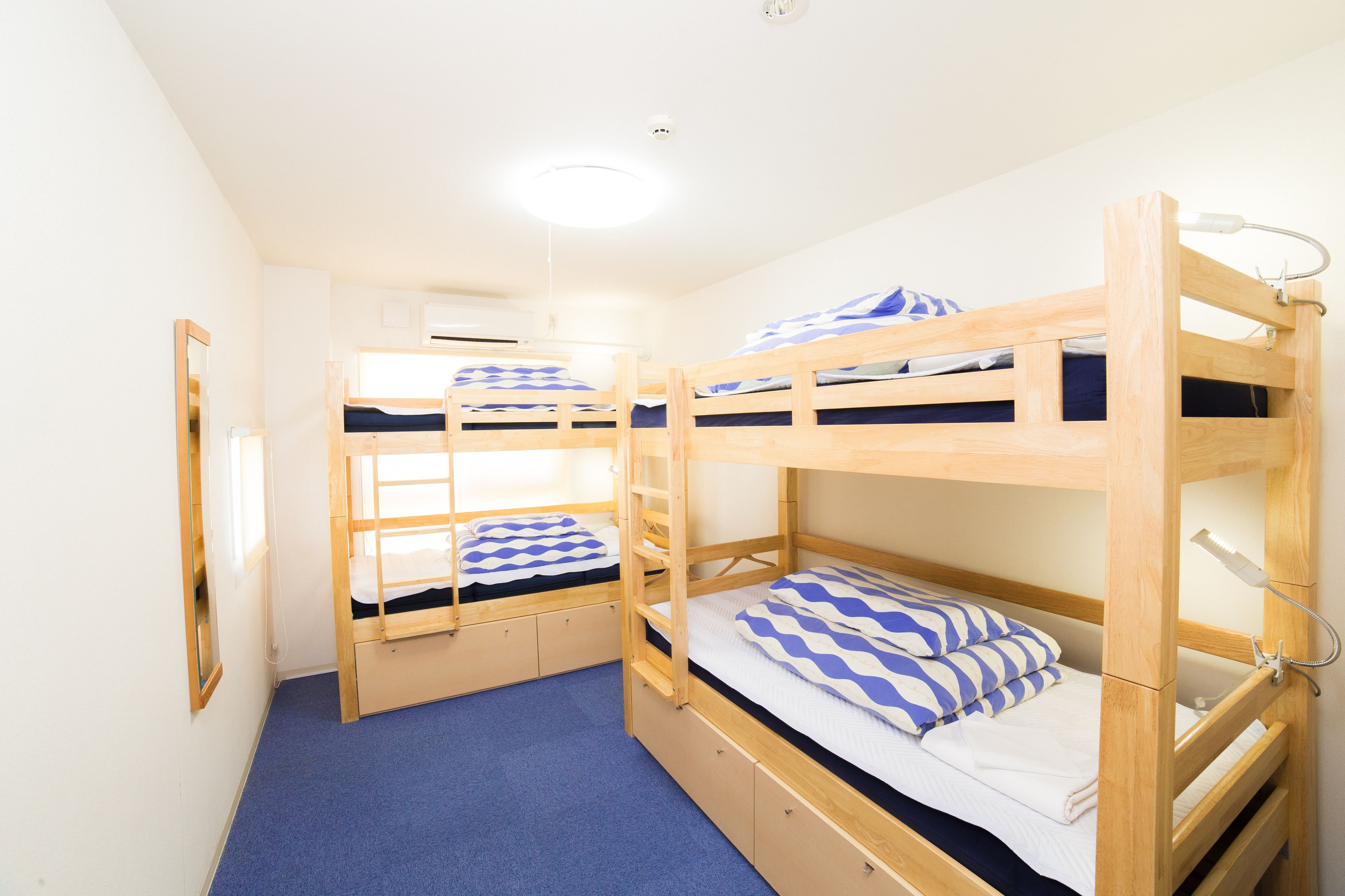Une chambre avec des lits superposés, un tapis bleu, des lits superposés en bois et un miroir au mur.