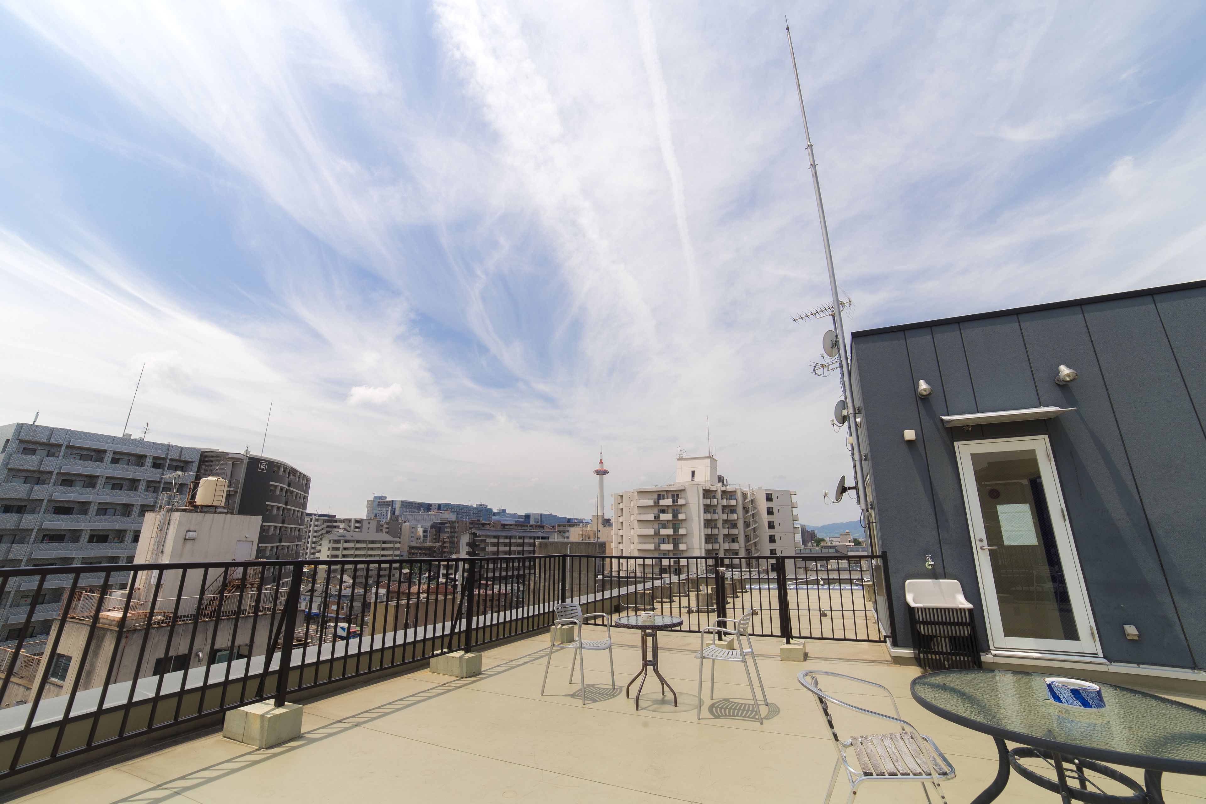 A rooftop terrace with a table and chairs, a small trash bin, and a door.