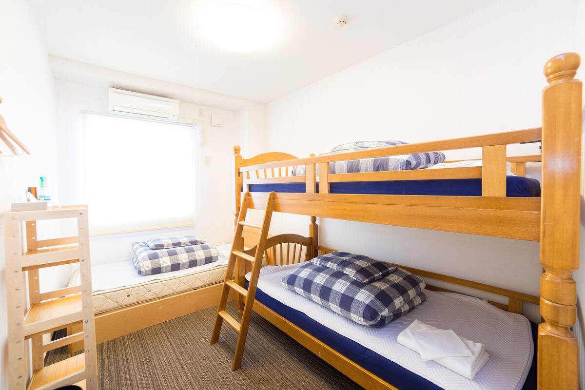 A bunk bed room with a ladder, a small desk, and a window.