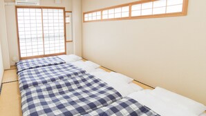 Um quarto com piso de esteira de tatame, porta deslizante shoji e cama com colcha xadrez azul e branco.