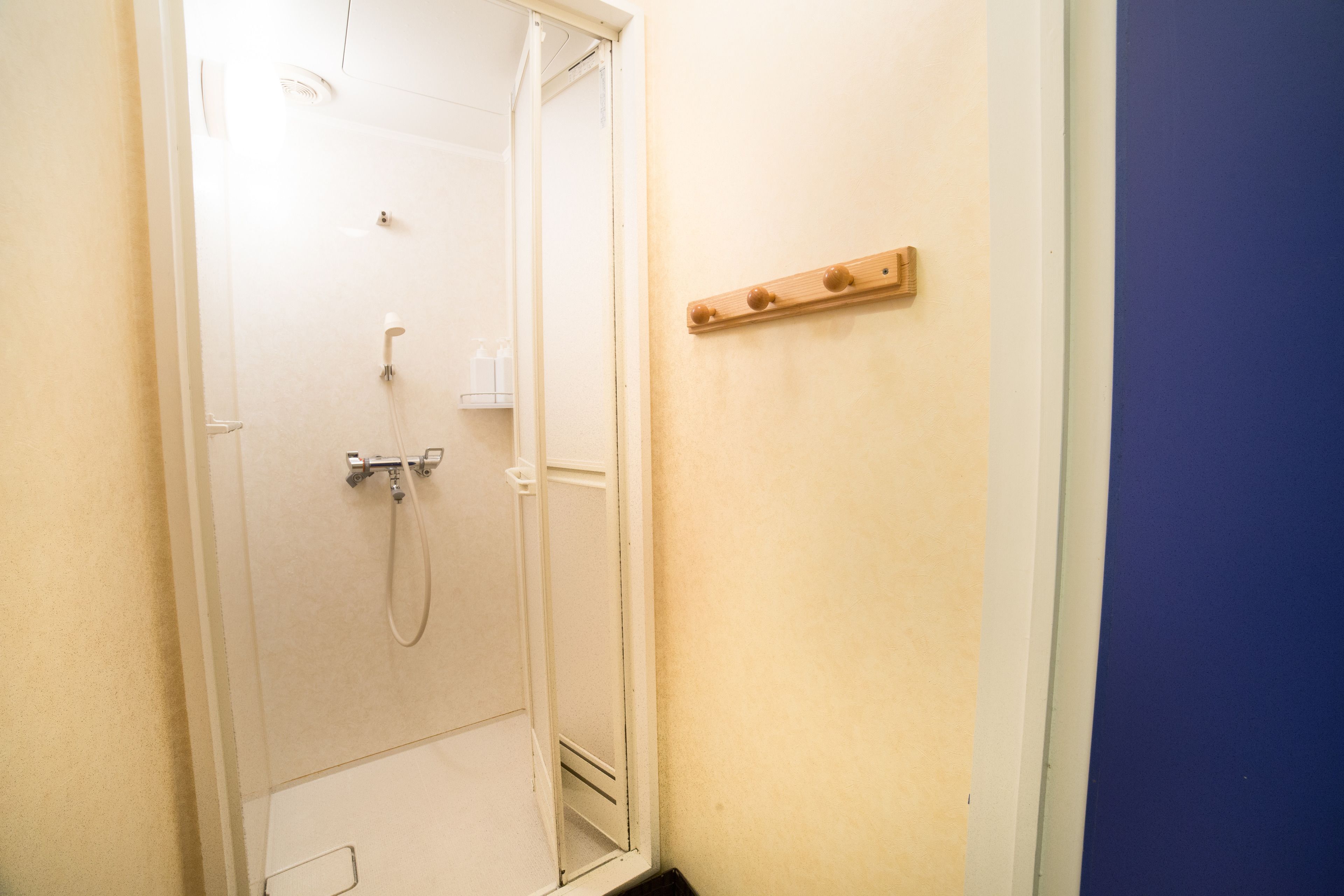 A bathroom with a shower, a mirror, and a wooden shelf with three knobs.