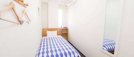 A small, neatly arranged bedroom with a bed, a wooden headboard, a mirror, and a wall-mounted coat rack.