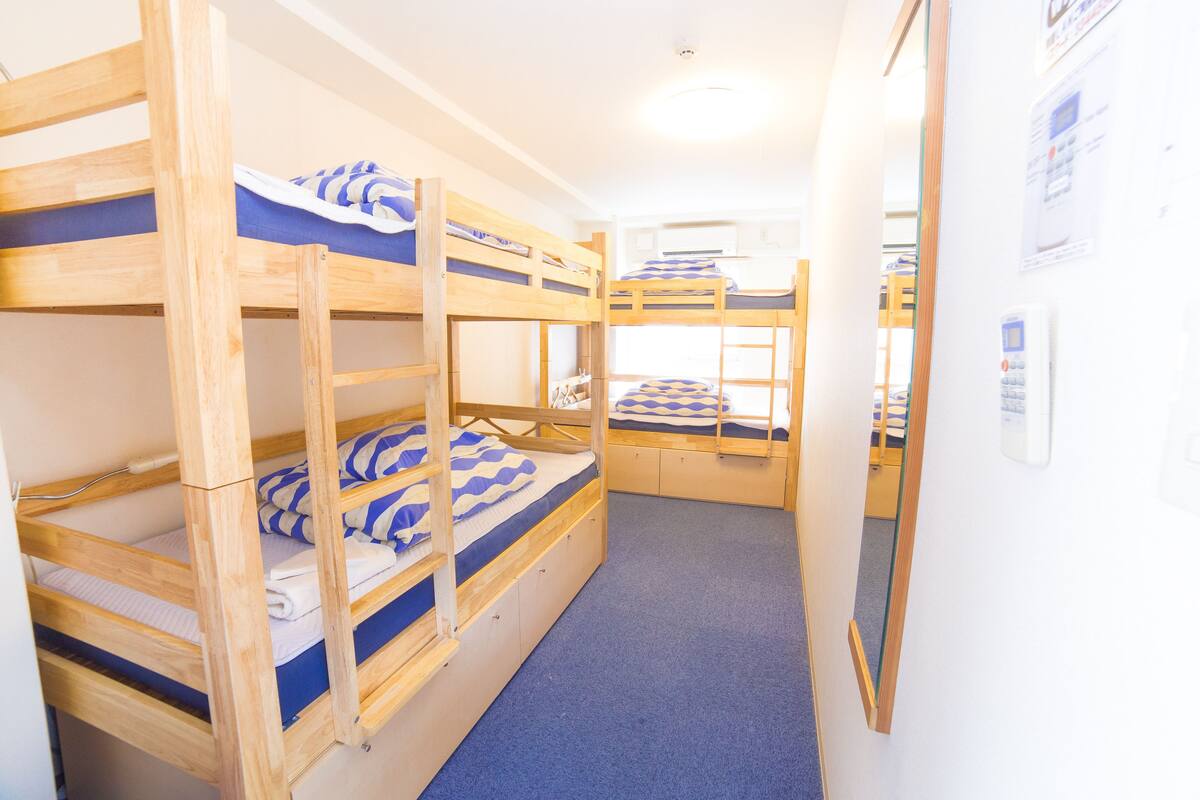 A bunk room with three bunk beds, a blue carpet, and a white wall with a thermostat.