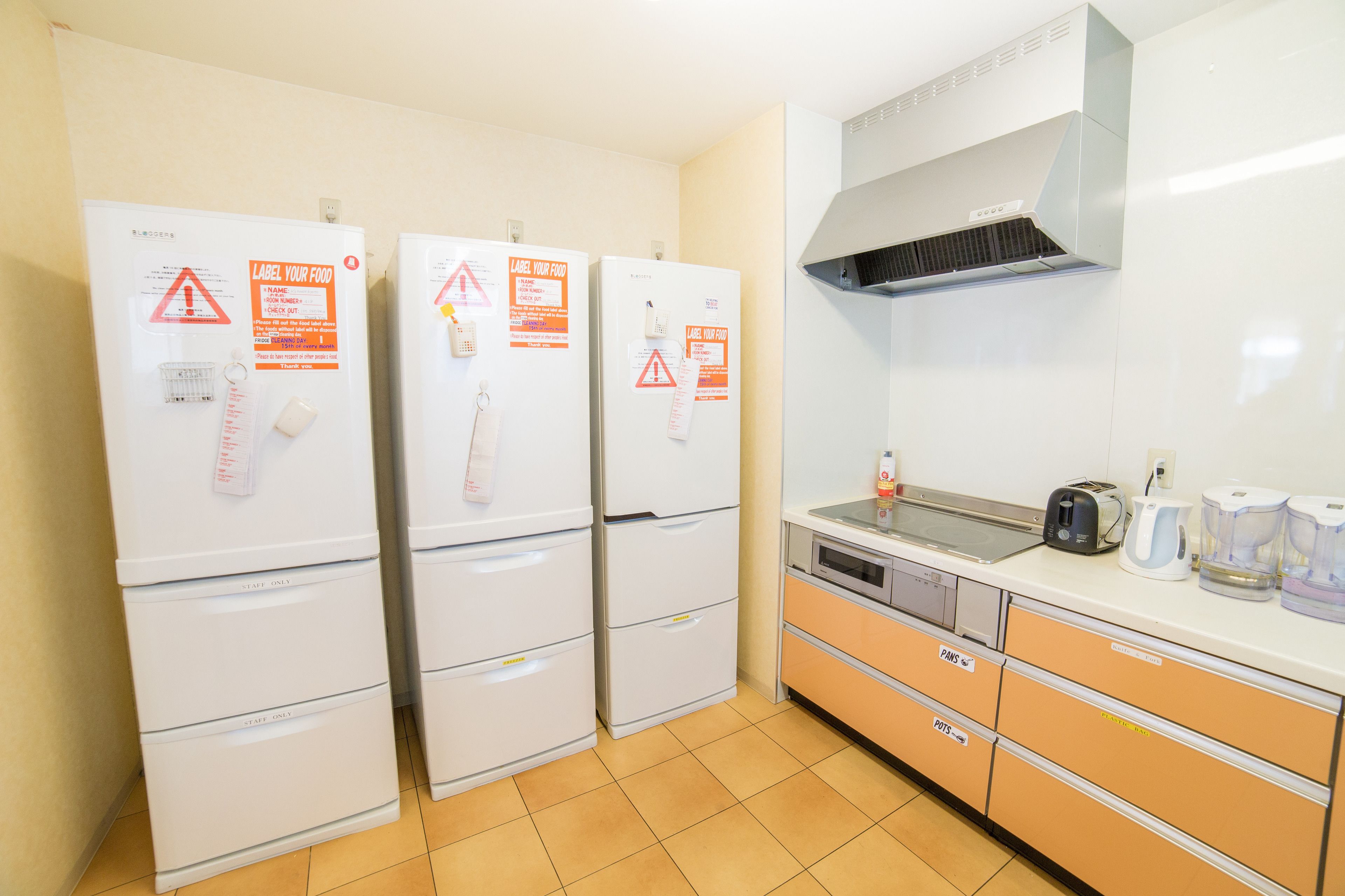 A kitchen with three white refrigerators, a microwave, and a coffee maker on the counter.