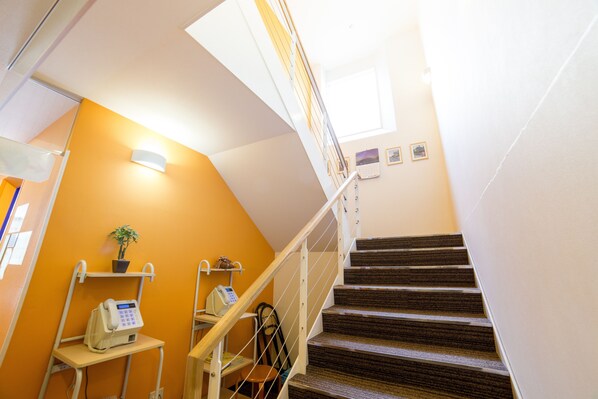 A staircase with a handrail, a wall-mounted phone, a small table with a plant, and a chair. - K's House Kyoto - Hostel (Kyoto)