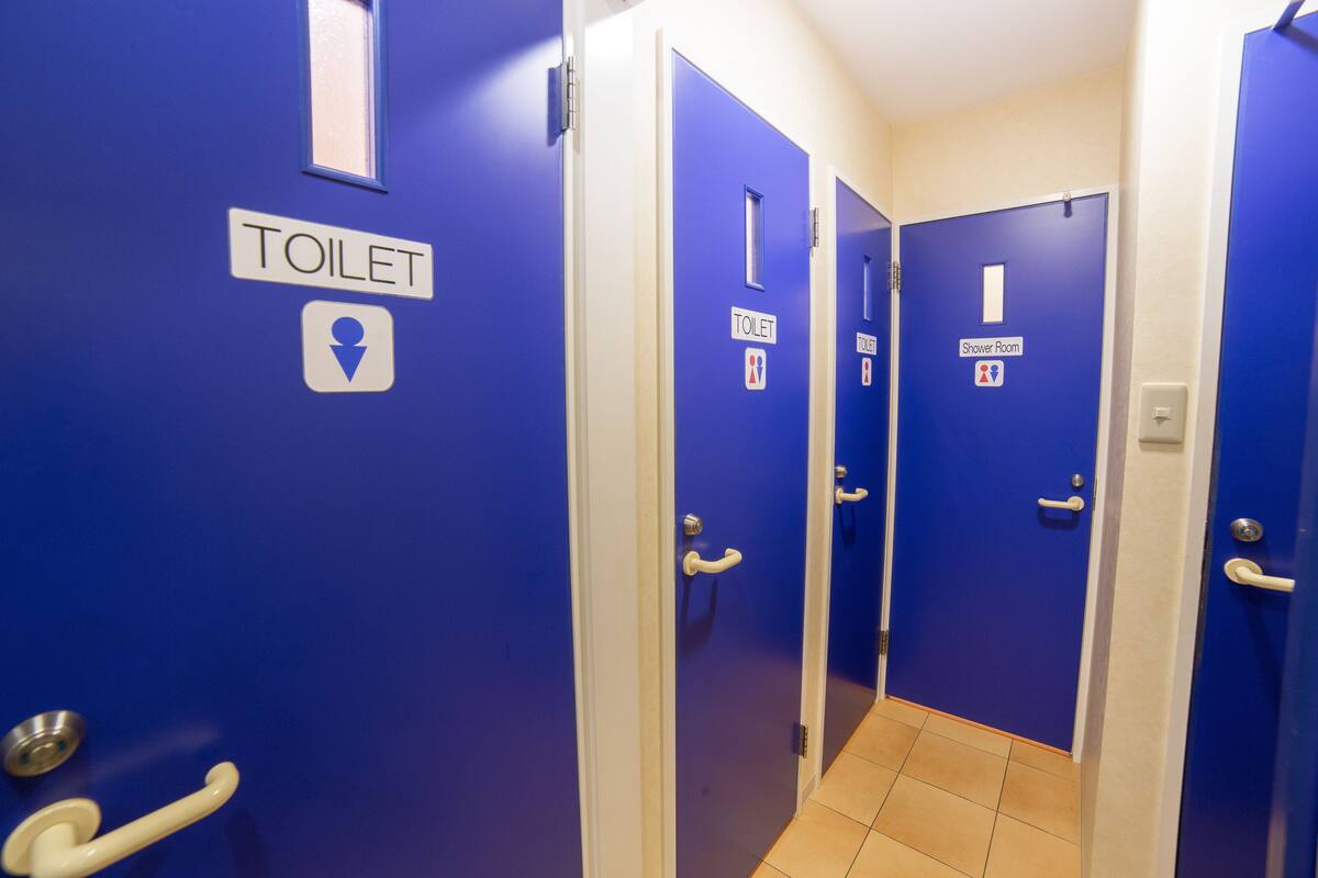 En korridor med blå døre, hver mærket med et toilet-skilt og et brusebads-skilt.