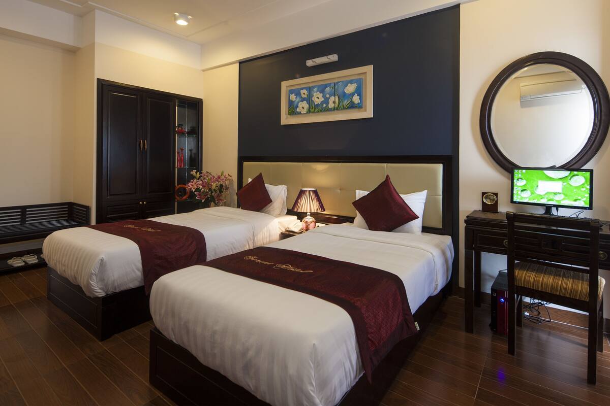 A hotel room with two beds, a desk with a computer, a chair, a mirror, and a painting on the wall.