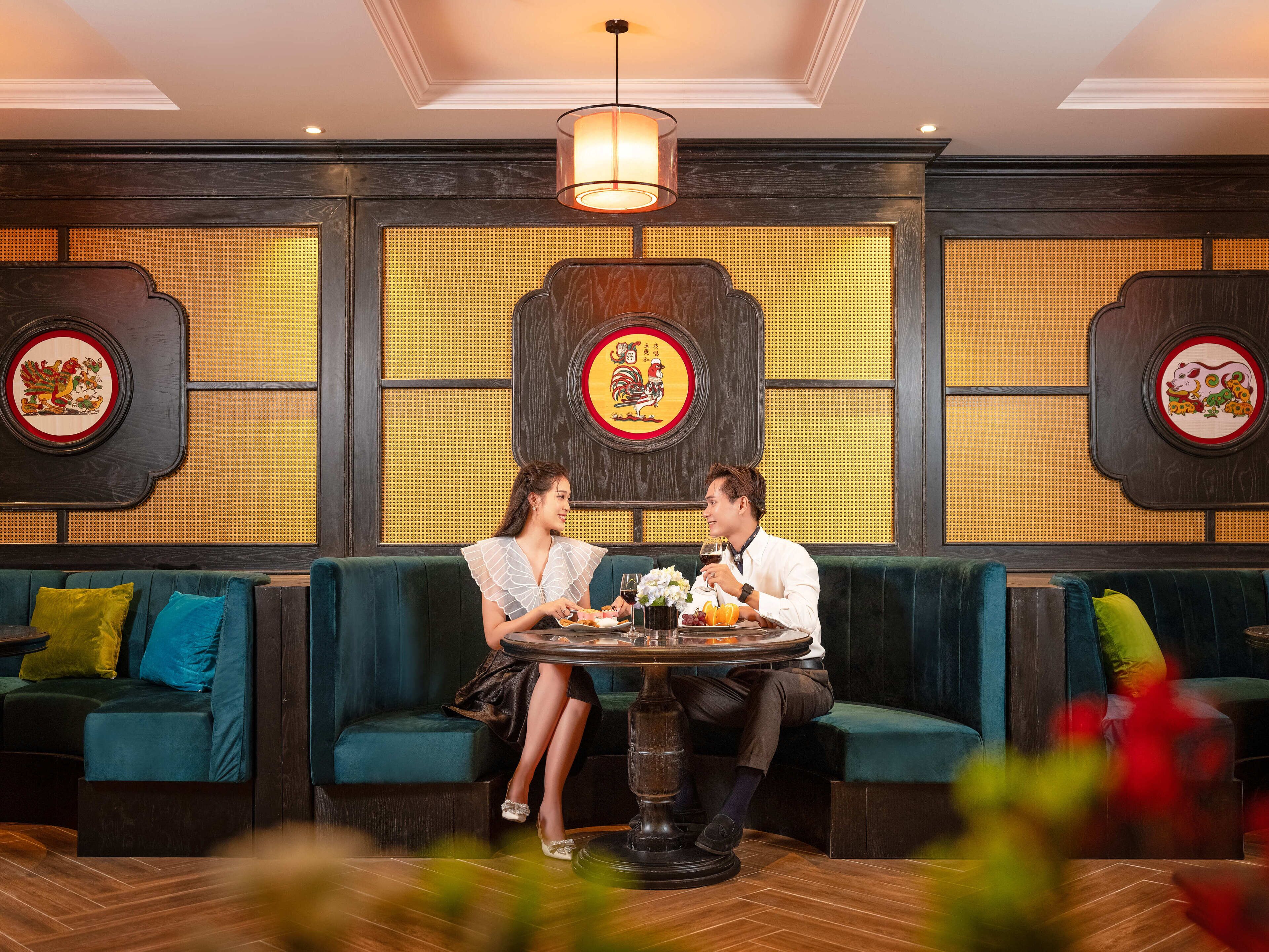 A couple dining at a table in a restaurant with traditional decor, including wall-mounted artwork and a patterned wall.