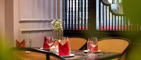 Une table à manger dressée avec des serviettes rouges, des verres transparents et un vase rempli de fleurs.